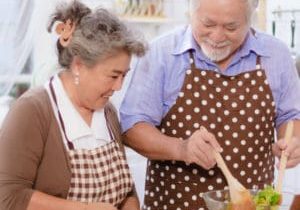 Square image of older couple preparing a salad